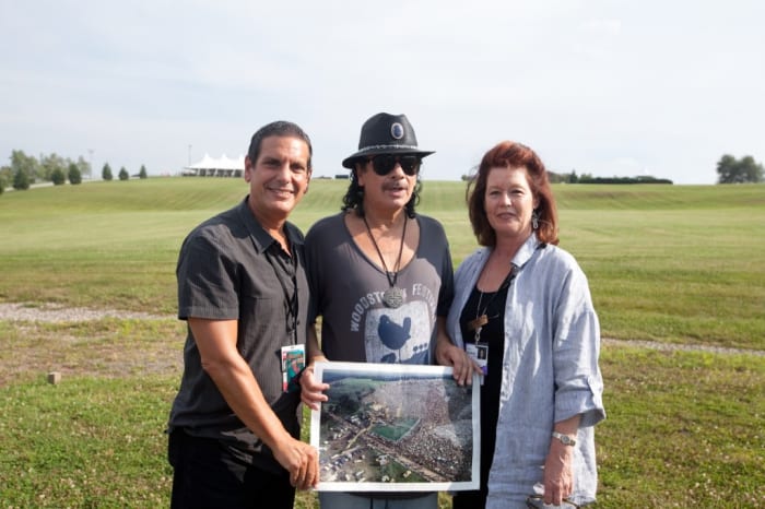 Before his sold out show Carlos Santana poses at the site of the 1969 Woodstock festival at Bethel Woods Center for the Arts, with Jason Stone Vice President-General Manager of Live Nation and Darlene Fedun COO of Bethel Woods. Photo courtesy of Michael Bloom for Bethel Woods.