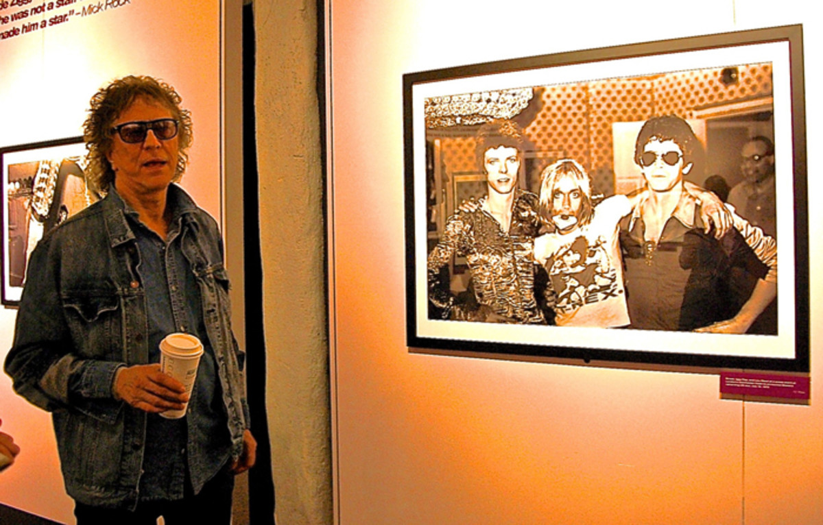  Mick Rock standing next to his famous Bowie/Pop/Reed photo